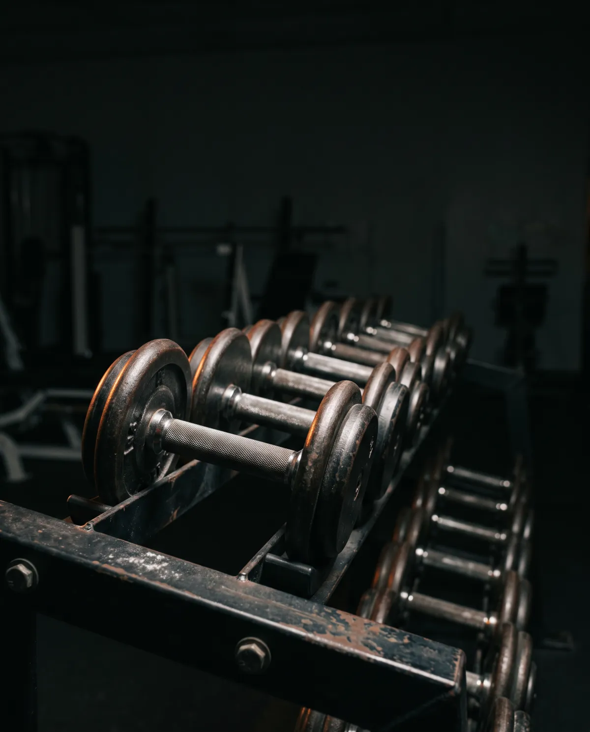 A rack of iron dumbbells lit by a single warm lamp